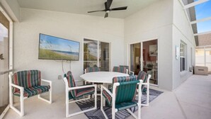 A covered patio with a white table and chairs, a ceiling fan, and a painting of a beach scene. - 4Bed3bath -  Mario kingdom Getaway (Davenport)