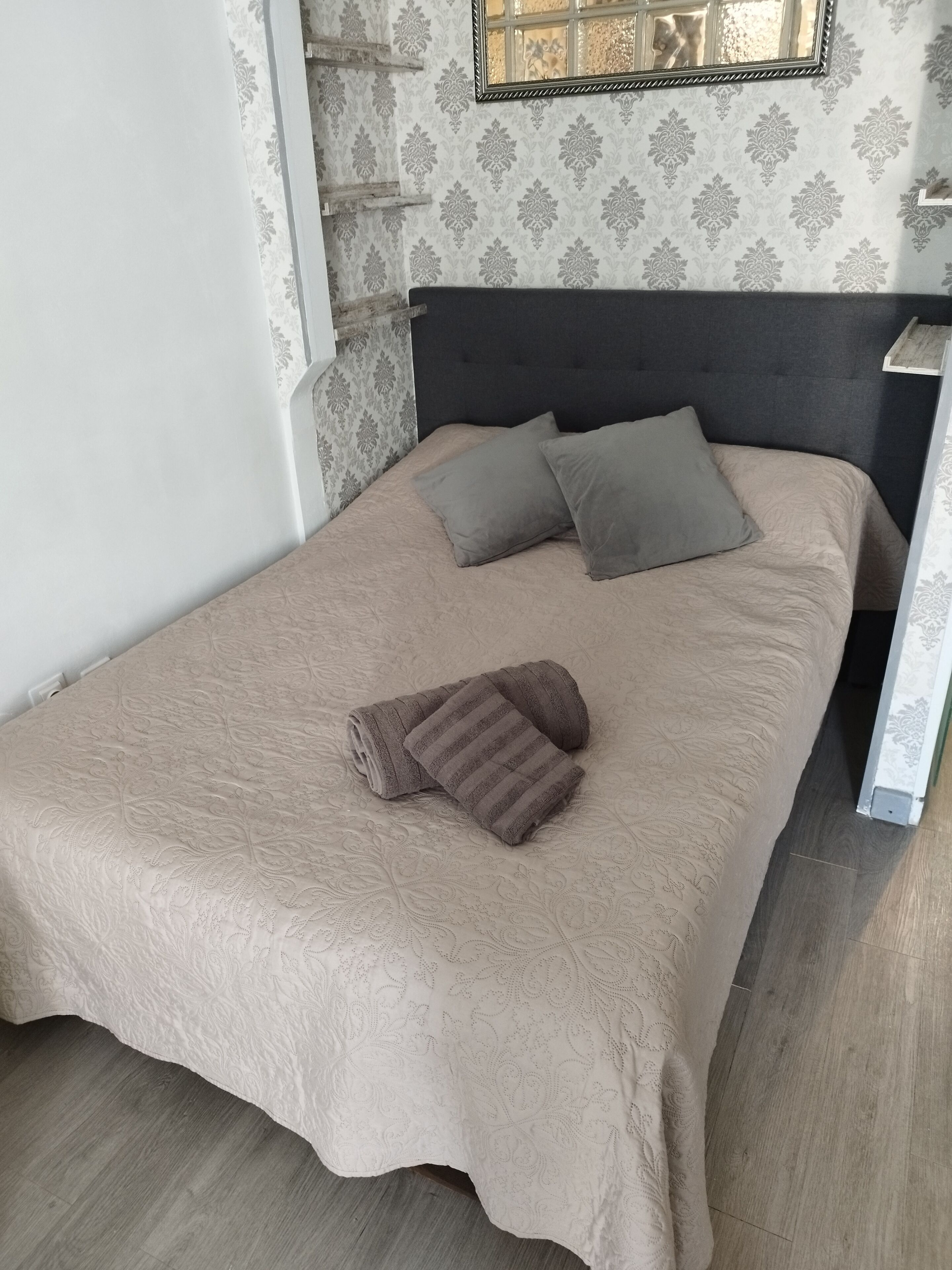 Una cama bien hecha con una colcha color beige, dos almohadas y una toalla enrollada.