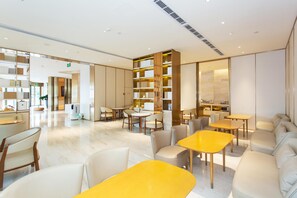 A modern hotel lobby with seating areas, a reception desk, and a large bookshelf.