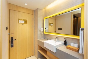 A modern bathroom with a wooden door, a white sink, a mirror with a yellow frame, and a towel rack.