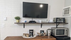 A kitchenette with a flat-screen TV, microwave, toaster, coffee maker, and a wooden cabinet with drawers.