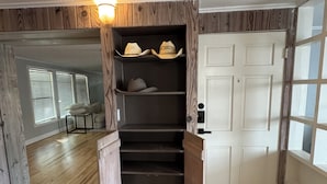 A room with a wooden floor, a white door, and a shelf with hats. - Luxury West 7th Fort Worth Stay - Balcony • W/D (Fort Worth)