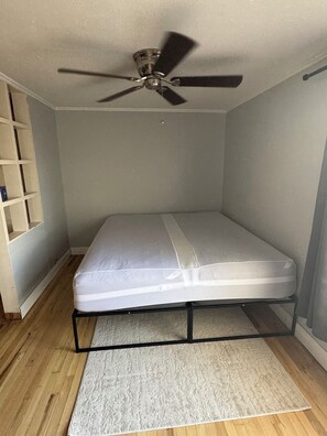 A small, single-bed room with a ceiling fan, a wooden floor, and a white mattress. - Luxury West 7th Fort Worth Stay - Balcony • W/D (Fort Worth)
