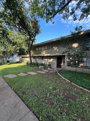 A building with a stone facade, a paved entrance, and a well-maintained lawn with stepping stones. - Luxury West 7th Fort Worth Stay - Balcony • W/D (Fort Worth)