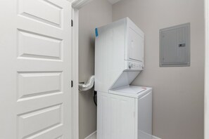 Een wasserette met een voorlader wasmachine en droger, een ventilatieslang en een gasmeter aan de muur.