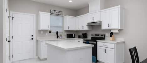 Una cocina moderna con armarios blancos, una isla central, horno empotrado y microondas.