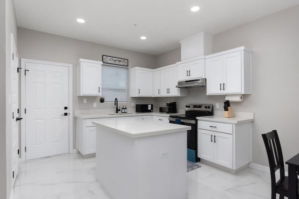 A modern kitchen with white cabinetry, a central island, a built-in oven, and a microwave.