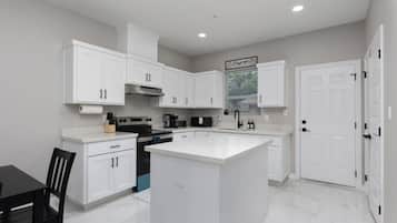 Une cuisine moderne avec des meubles blancs, un îlot central et un coin repas comprenant une table et des chaises.