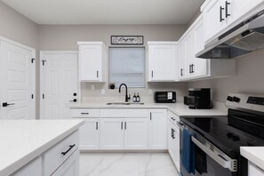 A modern kitchen with white cabinets, a black faucet, a microwave, a coffee maker, and a stove.