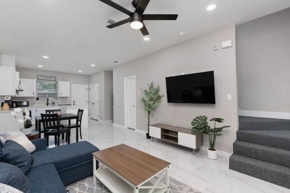 A modern living room with a sofa, coffee table, TV, and a staircase.