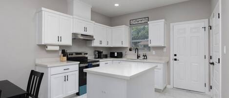 Una cocina moderna con armarios blancos, una isla central y una zona de comedor con mesa y sillas.