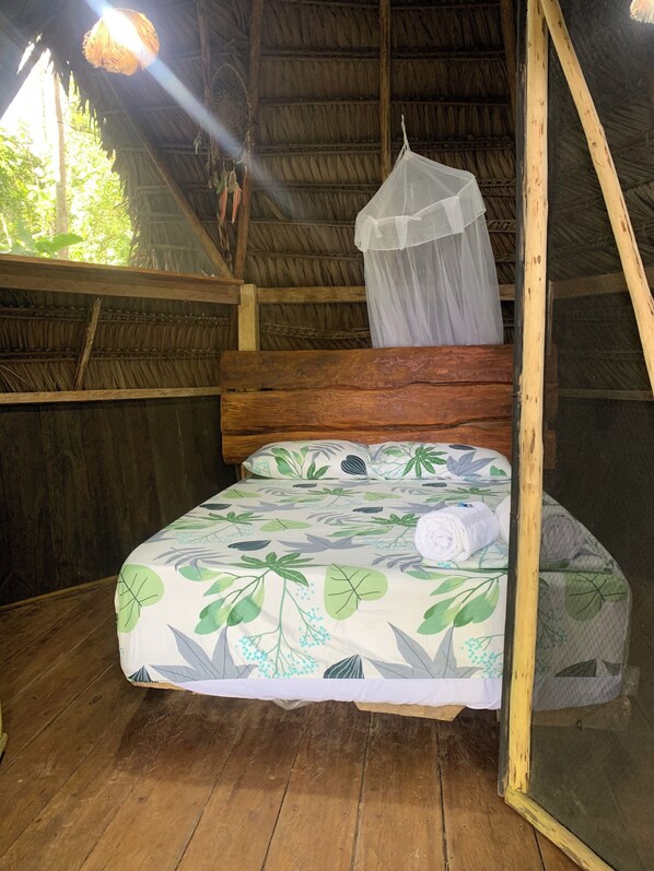 Un lit simple avec une couvre-lit à motifs de feuilles, une moustiquaire et une structure de plafond en bois.