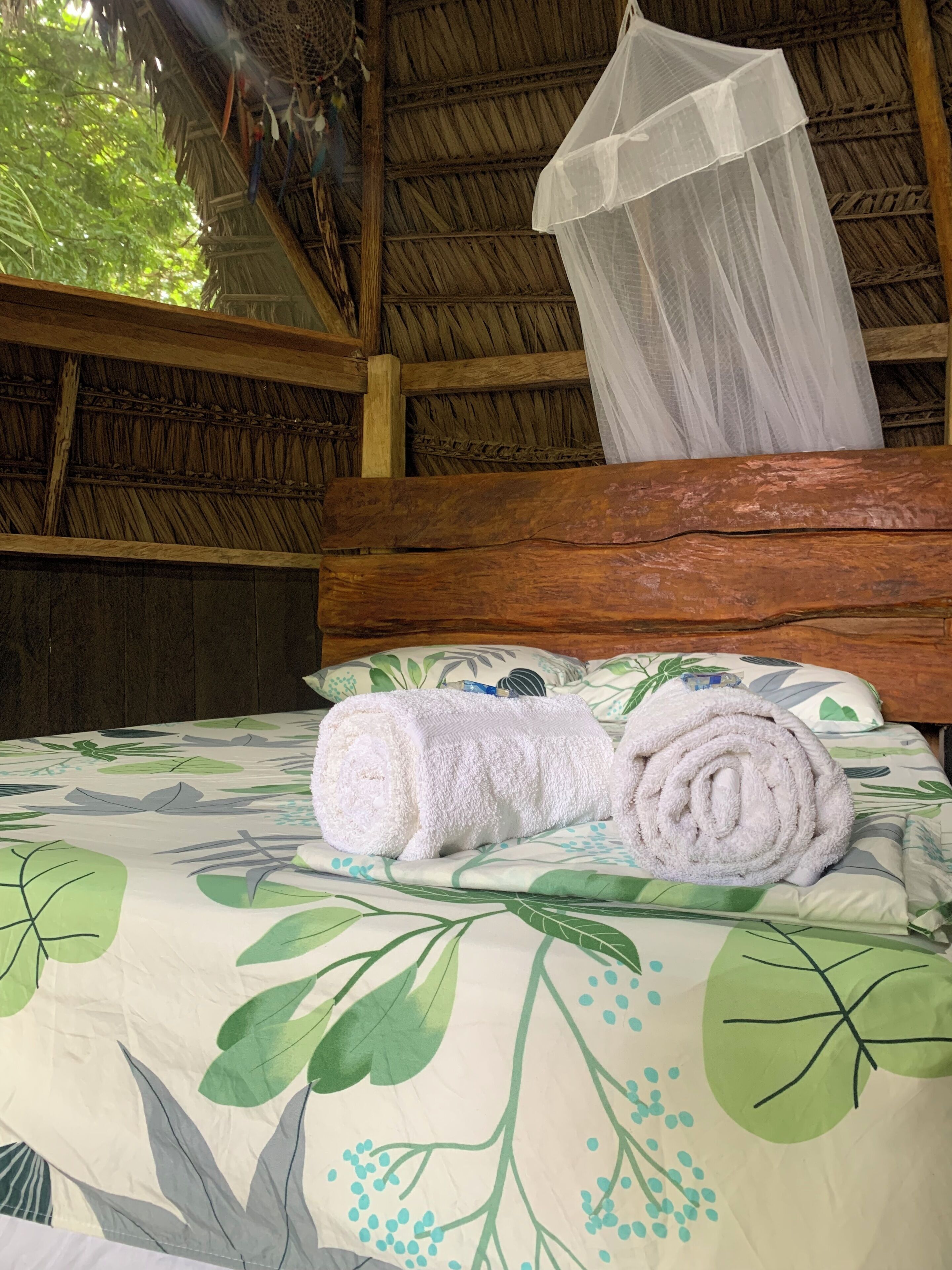 Ein Bett mit Moskitonetz, einer aufgerollten Handtuch und einer blumigen Tagesdecke.