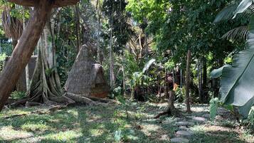 A lush garden with a variety of trees, a large mushroom, and a thatched structure.