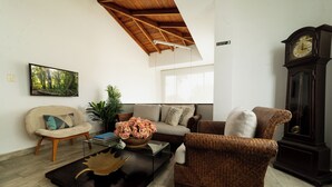 A living room with a sofa, armchairs, a coffee table, a clock, and a painting on the wall.