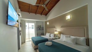 A hotel room with two beds, a ceiling fan, a TV, and a balcony with a view of the beach.