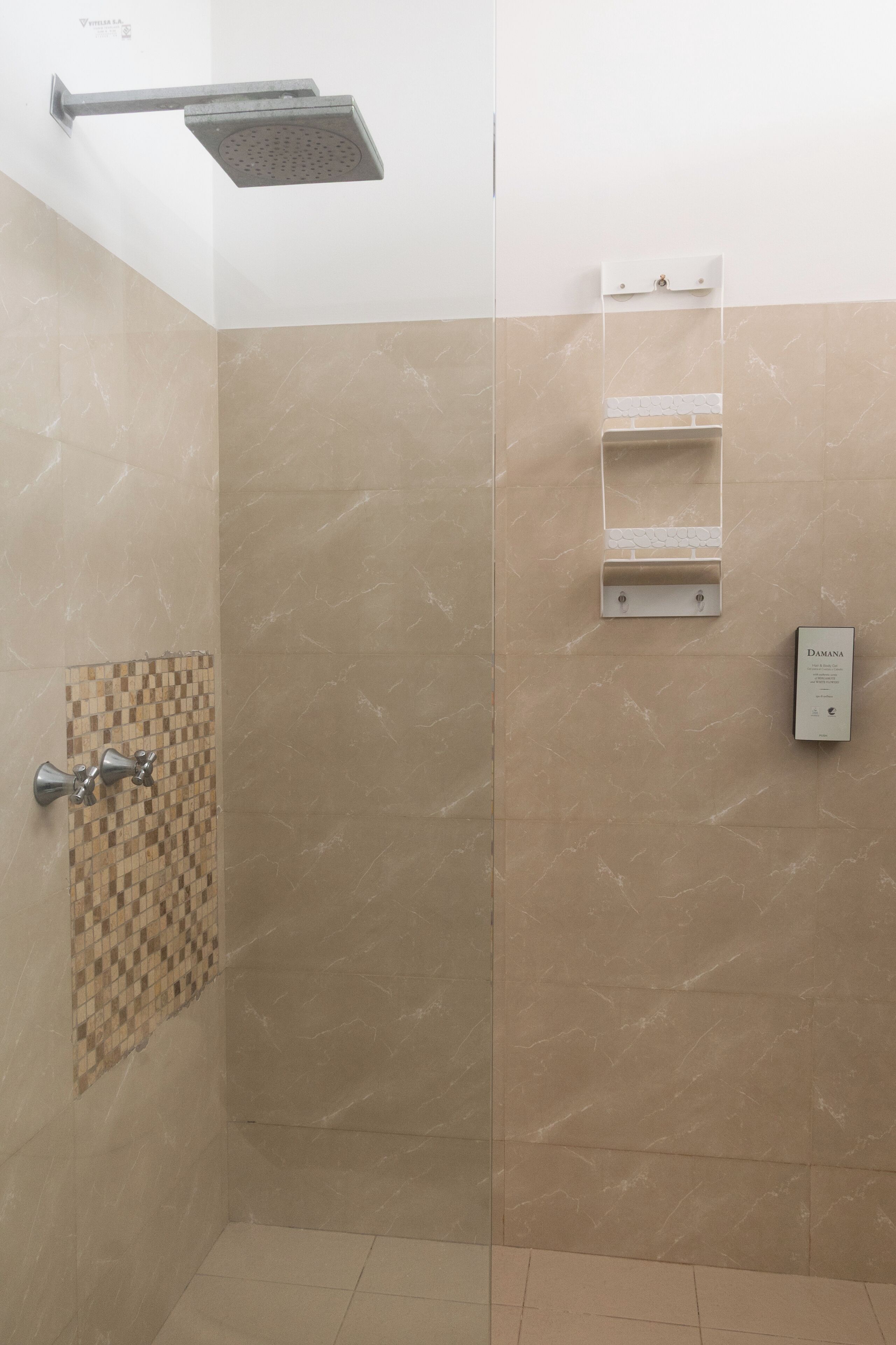 Une douche équipée d’un pommeau de douche à main, un mur carrelé avec un motif à carreaux et un panneau de commande.