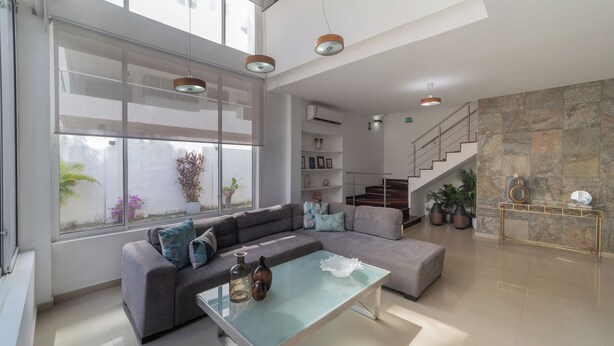 A modern living room with a sectional sofa, a glass coffee table, and a staircase leading to an upper level.