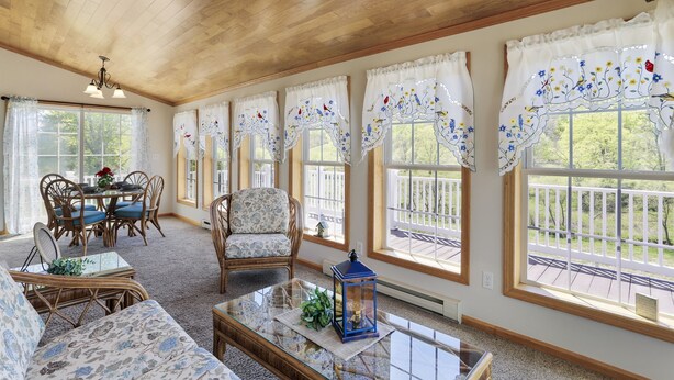 Une pièce dotée d’un plafond en bois, de grandes fenêtres ornées de rideaux décoratifs, de meubles en osier et d’une table basse en verre.
