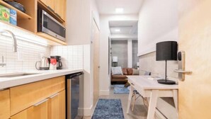 A compact kitchen with wooden cabinets, a microwave, and a coffee maker. A dining area with a table and chairs is visible in the background. - Top of the Hill-Condotel on First Hill-Swedish (Seattle)