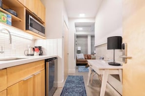 A compact kitchen with wooden cabinets, a microwave, and a coffee maker. A dining area with a table and chairs is visible in the background.