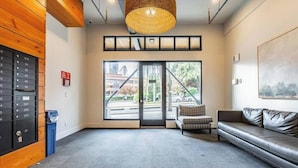 A reception area with a wooden wall, a black storage unit, a wicker ceiling light, a sofa, and a large window with a view of a bridge and trees. - Top of the Hill-Condotel on First Hill-Swedish (Seattle)