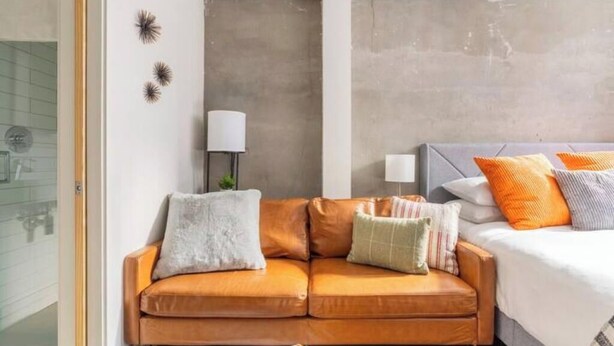 A modern hotel room with a sofa, a bed with multiple pillows, a lamp, and decorative wall art. - Top of the Hill-Condotel on First Hill-Swedish (Seattle)