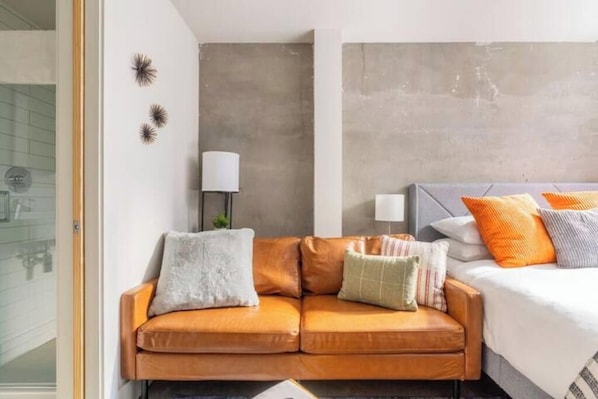 A modern hotel room with a sofa, a bed with multiple pillows, a lamp, and decorative wall art.