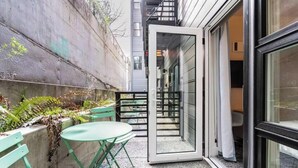 Un pequeño espacio al aire libre con una mesa y sillas, un muro de concreto y una puerta de vidrio que da a un edificio.