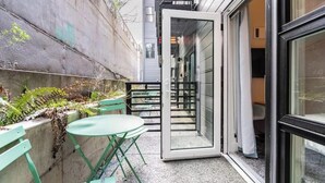 A small outdoor seating area with a table and chairs, a concrete wall, and a glass door leading to an interior space. - Broadway-Condotel on First Hill (Seattle)