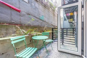 A small outdoor seating area with two green metal chairs and a table, a concrete wall with some greenery, and a glass door leading to a staircase. - Broadway-Condotel on First Hill (Seattle)