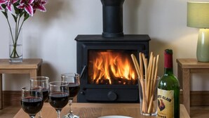 Una habitación acogedora con una estufa de leña, copas de vino, un bol de frutos secos y una botella de vino.