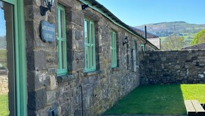 Una cabaña de piedra con contraventanas verdes y un letrero que dice 'Apple Blossom Cottage'.