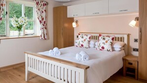 Un dormitorio ordenado con cama de madera, ropa de cama blanca y almohadas estampadas con motivos florales.