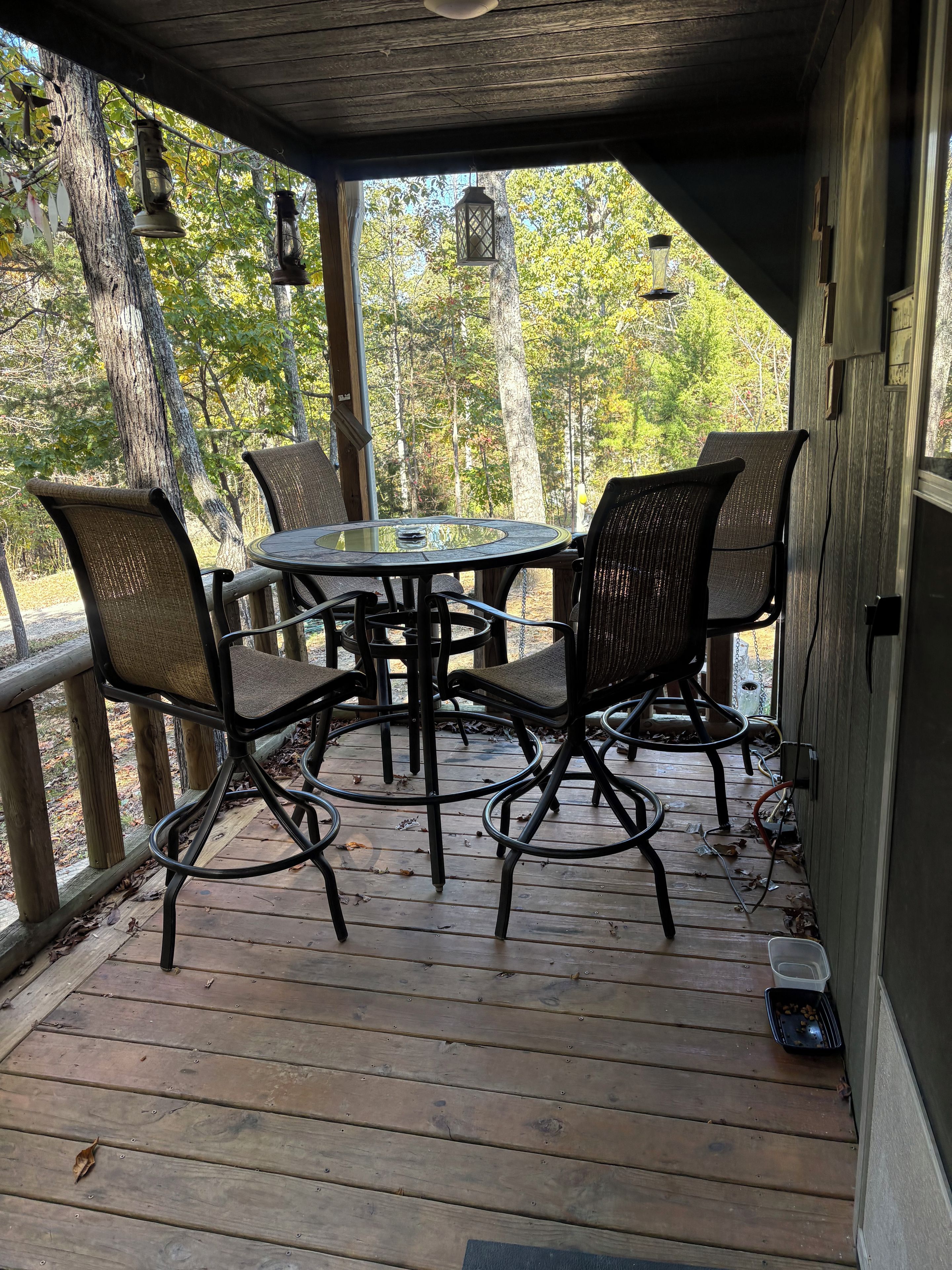 A wooden deck with a round table and four chairs, surrounded by trees.