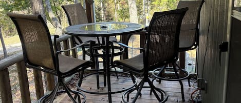 Eine Holzterrasse mit einem runden Tisch und vier Stühlen, umgeben von Bäumen.