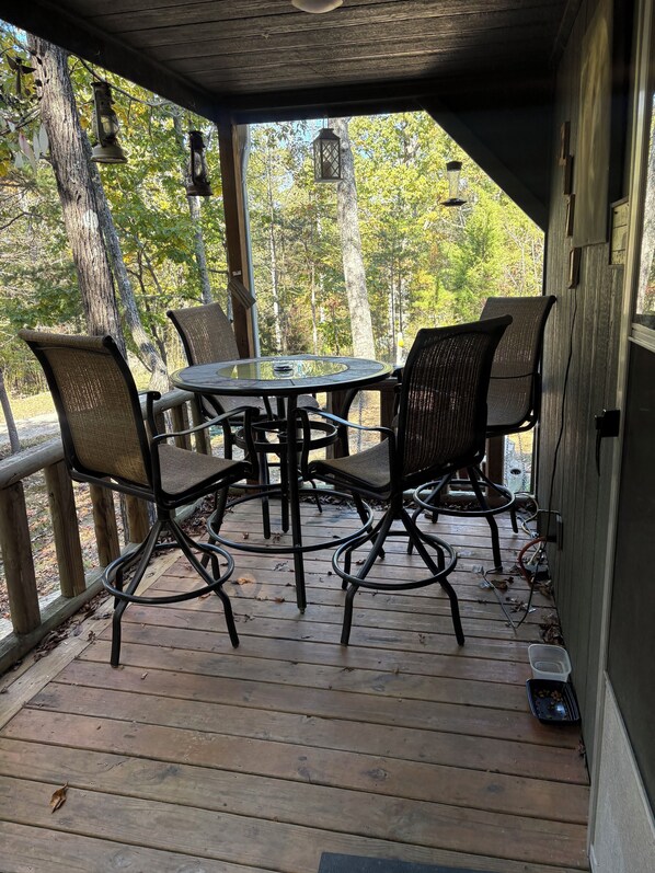 A wooden deck with a round table and four chairs, surrounded by trees.