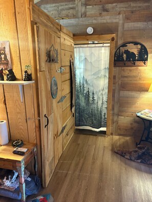 A wooden cabin interior with a cabin sign, a mountain-themed curtain, and a bear decoration on the wall.
