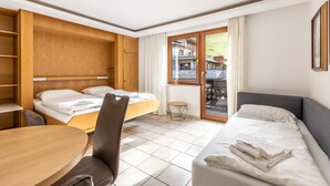 A hotel room with a bed, a sofa, a table, and a chair. There is a window with a view of a building outside.