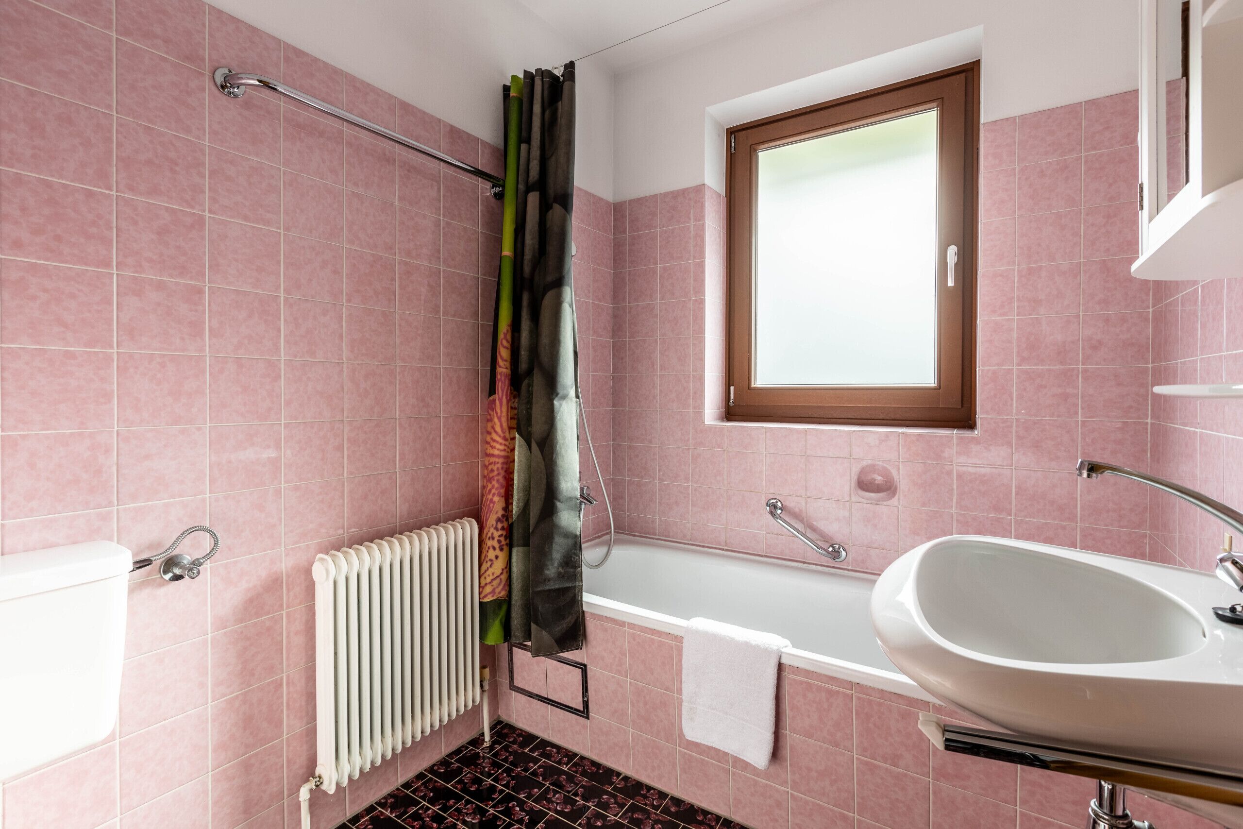 A bathroom with pink tiles, a white sink, a bathtub, a window, and a shower curtain.