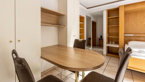 A compact room with a wooden dining table, two chairs, a bed with a wooden headboard, and built-in shelving.