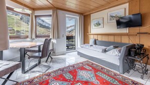 Et moderne værelse med træloft, et stort vindue med udsigt til bjerge, en grå sofa, et spisebord med stole og et fjernsyn monteret på væggen.