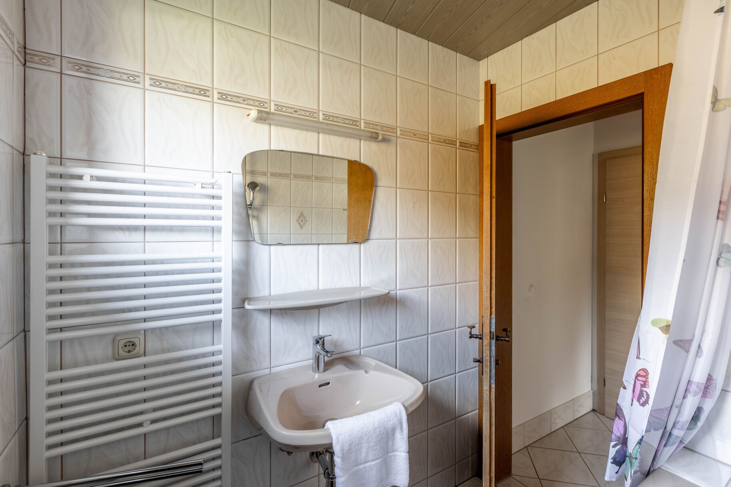 A bathroom with a white sink, a mirror, and a towel hanging on the wall.