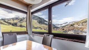 A dining area with a table and chairs, large windows with a view of a mountainous landscape and a town below.