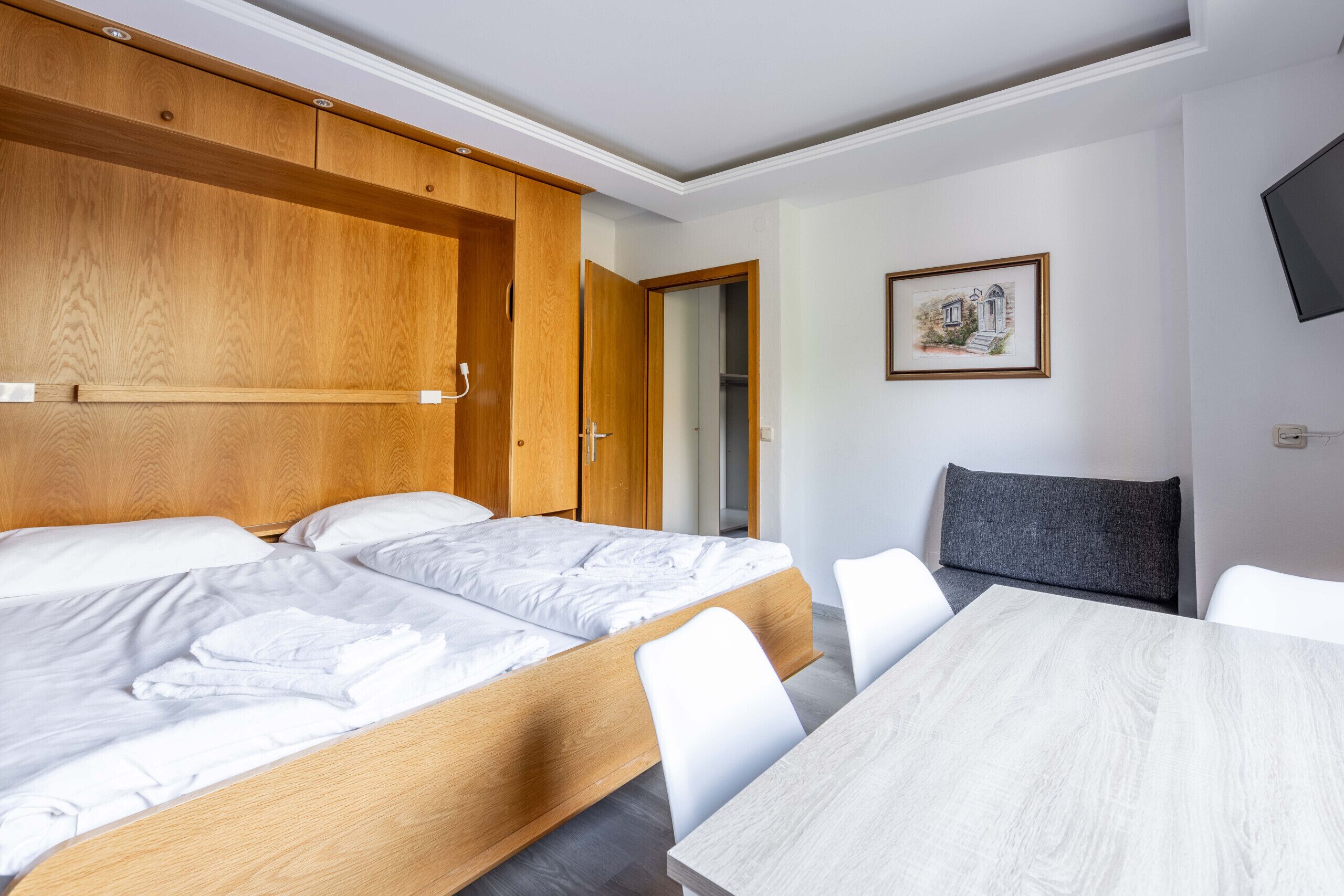 A hotel room with a wooden bed, a small table, and a grey chair.