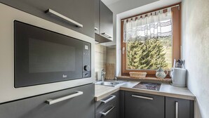 Moderni keittiö, jossa on sisäänrakennettu mikroaaltouuni, pesuallas ja ikkuna, josta avautuu näkymä puita kohti.