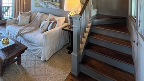 Un salón espacioso con techo alto, una escalera que sube a un nivel superior, un ventanal grande y un cuadro en la pared.