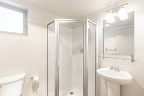 Ett badrum med en dusch som är avskärmad med glasväggar, ett vitt handfat och en spegel ovanför handfatet.