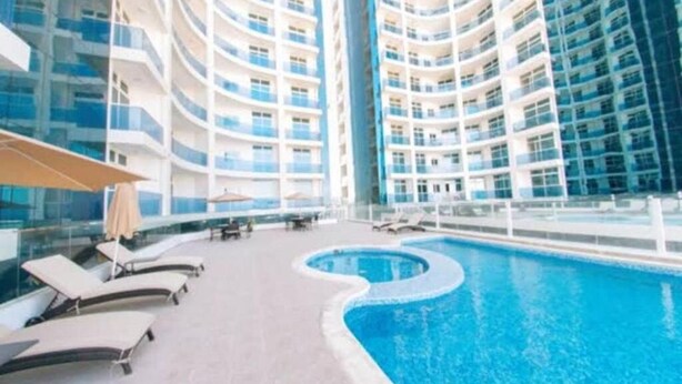 Un hotel moderno con una piscina curva, varios balcones y tumbonas.