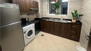 Cocina compacta con refrigerador, estufa, lavadora y una ventana con planta.